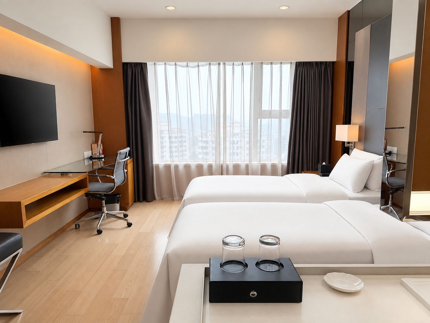 A hotel room with a bed, a desk, a chair, a TV, and a window with curtains.