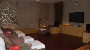 A modern living room with a flat-screen TV, a sofa, a coffee table, and a decorative wall panel. - Grand Mercure Dongguan Humen (Dongguan)