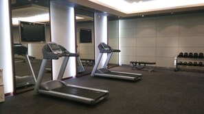 Une salle de sport équipée de tapis de course, d’un banc et d’un porte-haltères.