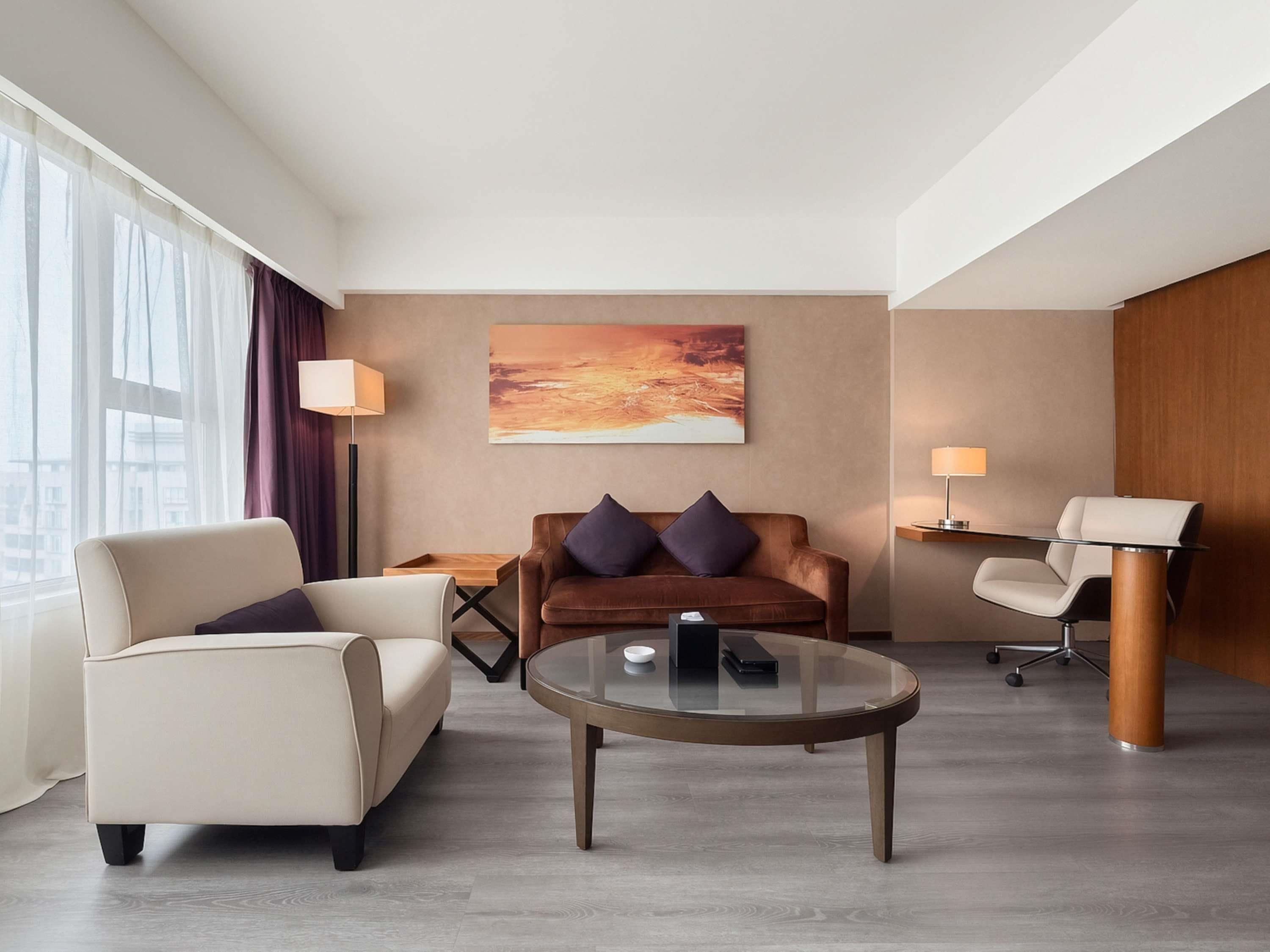 Una habitación de hotel moderna con sofá, sillón, mesita de centro y escritorio con silla.
