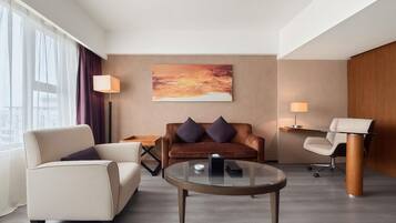 Et moderne hotelværelse med sofa, lænestol, sofabord og et skrivebord med stol.