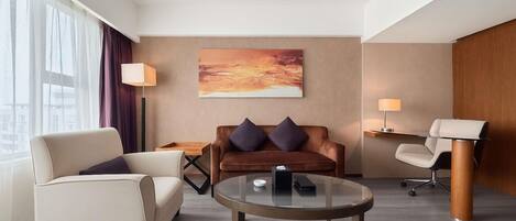 Una habitación de hotel moderna con sofá, sillón, mesita de centro y escritorio con silla.