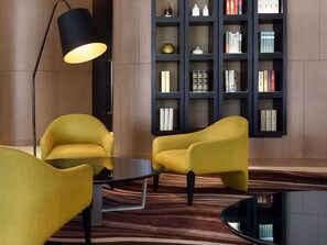 Une pièce moderne avec deux fauteuils jaunes, un lampadaire noir et une bibliothèque remplie de livres.