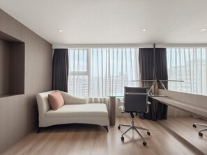 Een moderne hotelkamer met een gebogen bank, een bureau met stoel, en grote ramen met uitzicht op de stad.