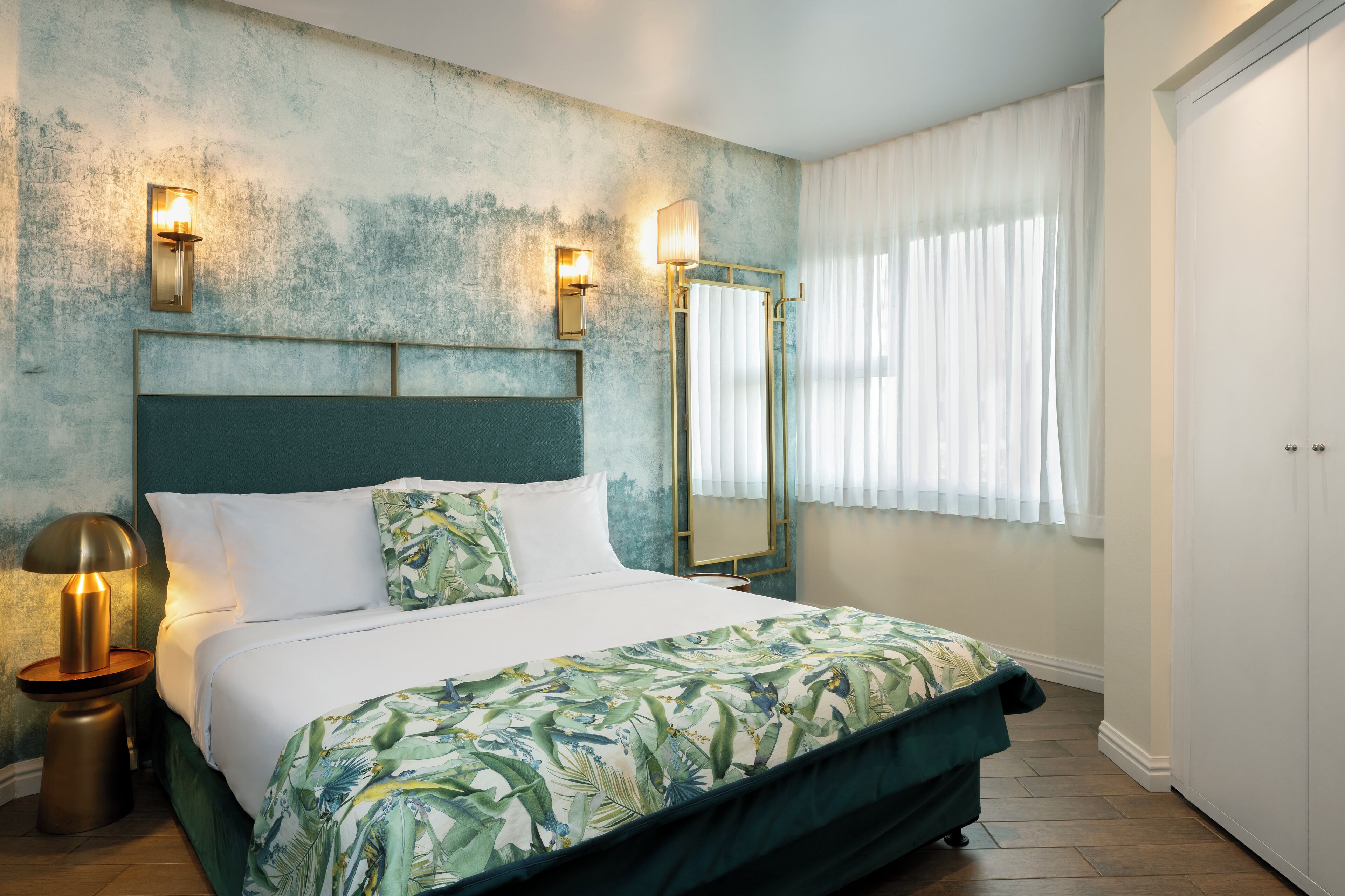 A neatly made bed with a green and white floral bedspread, a bedside lamp, and a wall-mounted light fixture.