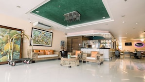 A spacious lobby with a green ceiling, a seating area with wicker furniture, and a bar area with a neon sign. - Allure Hotel & Suites (Mandaue)