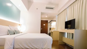 A hotel room with a bed, bedside table, TV, and a mirror. - Allure Hotel & Suites (Mandaue)