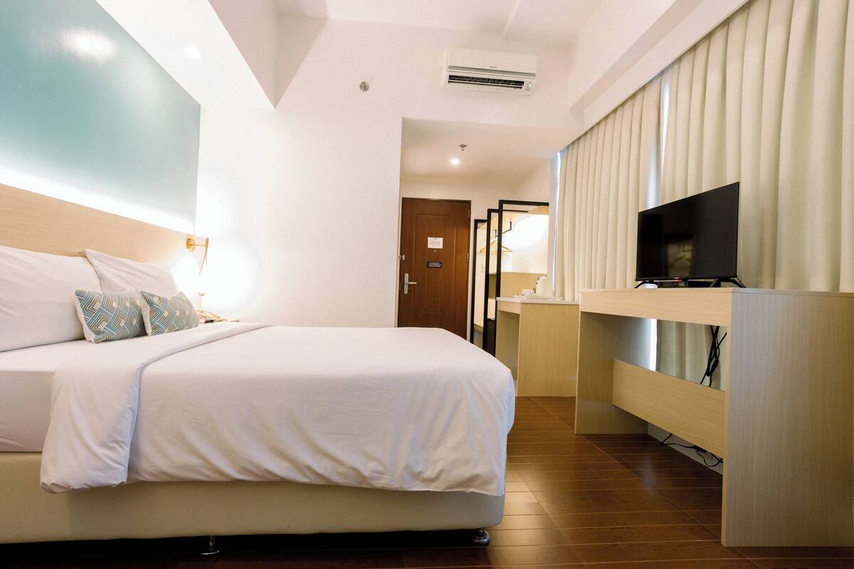 Habitación de hotel con cama, mesita de noche, televisor y espejo.