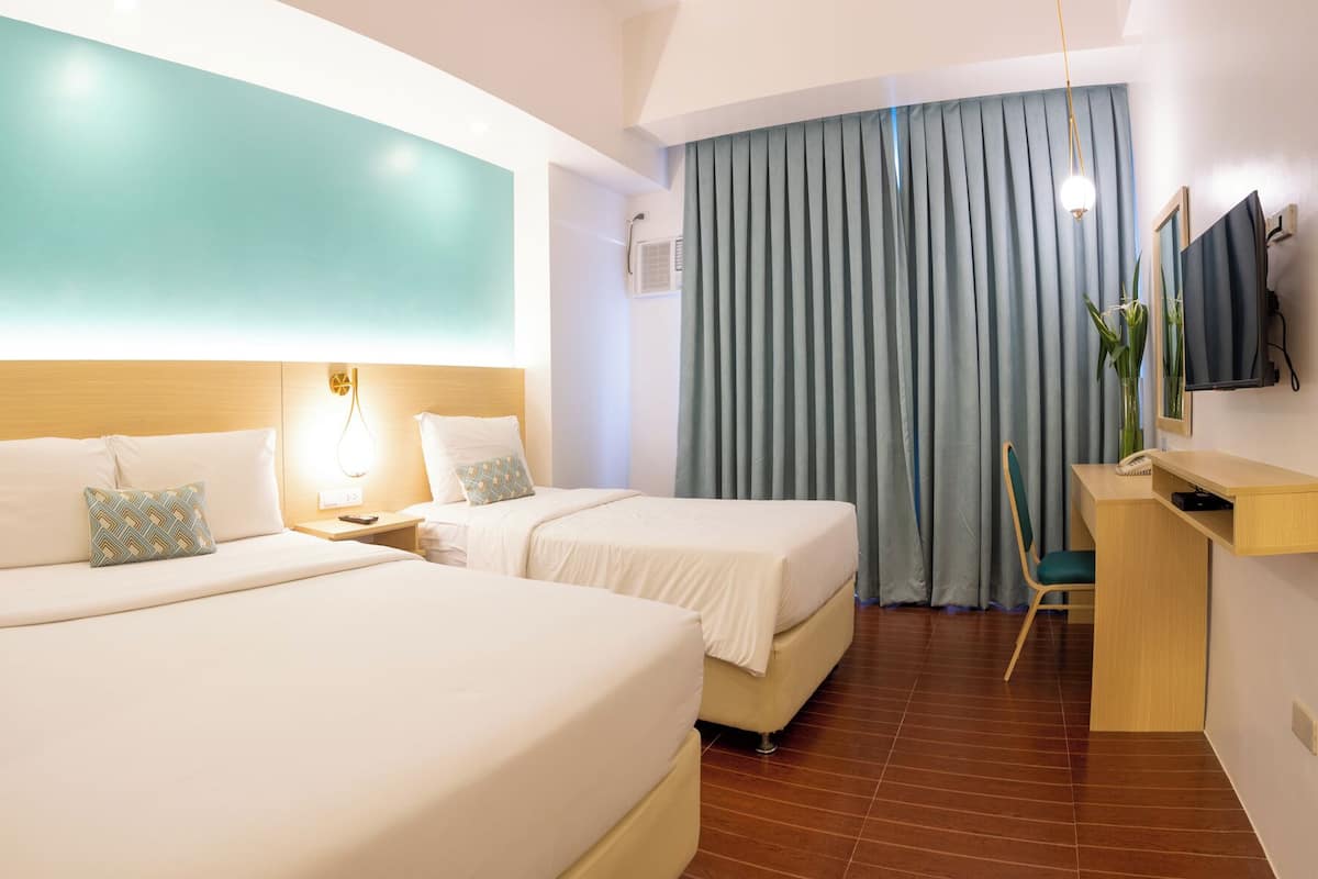 Habitación de hotel con dos camas, un escritorio, una silla, un televisor y un ventanal grande con cortinas.