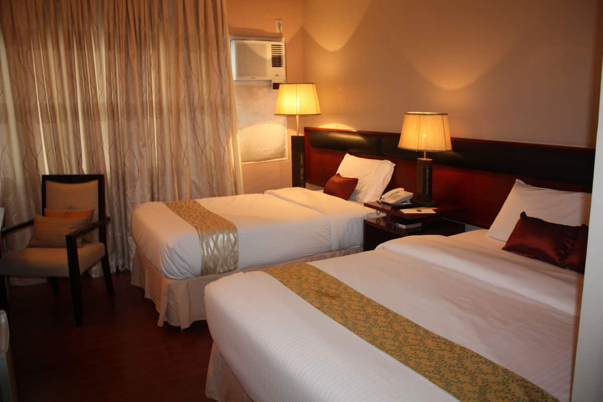 Una habitación de hotel con dos camas, una silla, una mesita de noche y una lámpara.