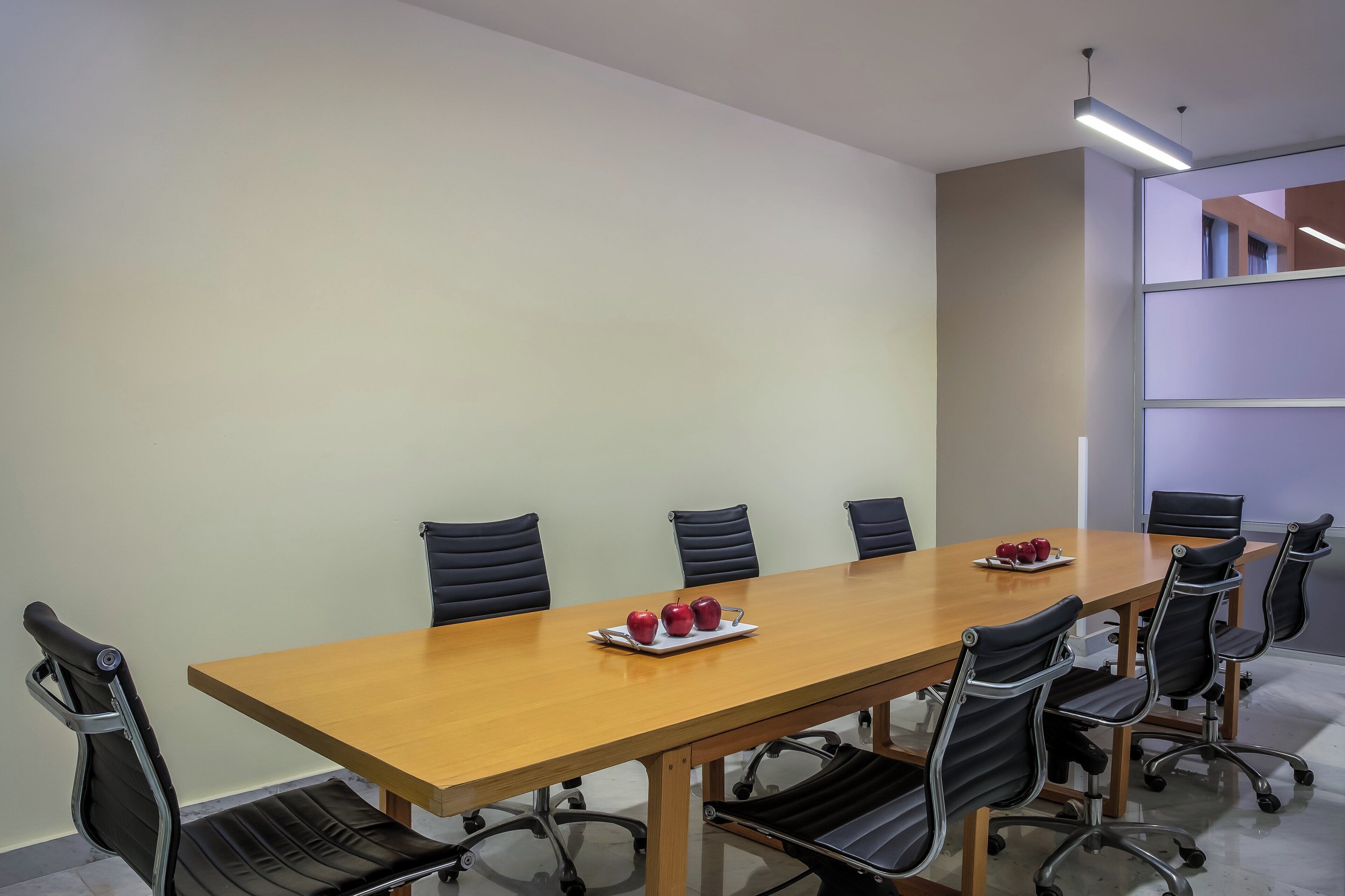 A conference room with a long wooden table, black leather chairs, and a tray of apples.