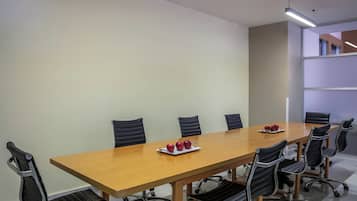 Une salle de conférence avec une longue table en bois, des fauteuils en cuir noir et un plateau de pommes.