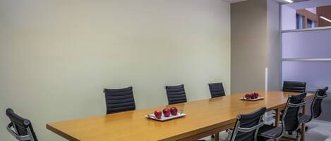 A conference room with a long wooden table, black leather chairs, and a tray of apples.