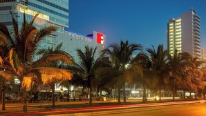 A modern building with a prominent red logo, surrounded by palm trees and a well-lit street.