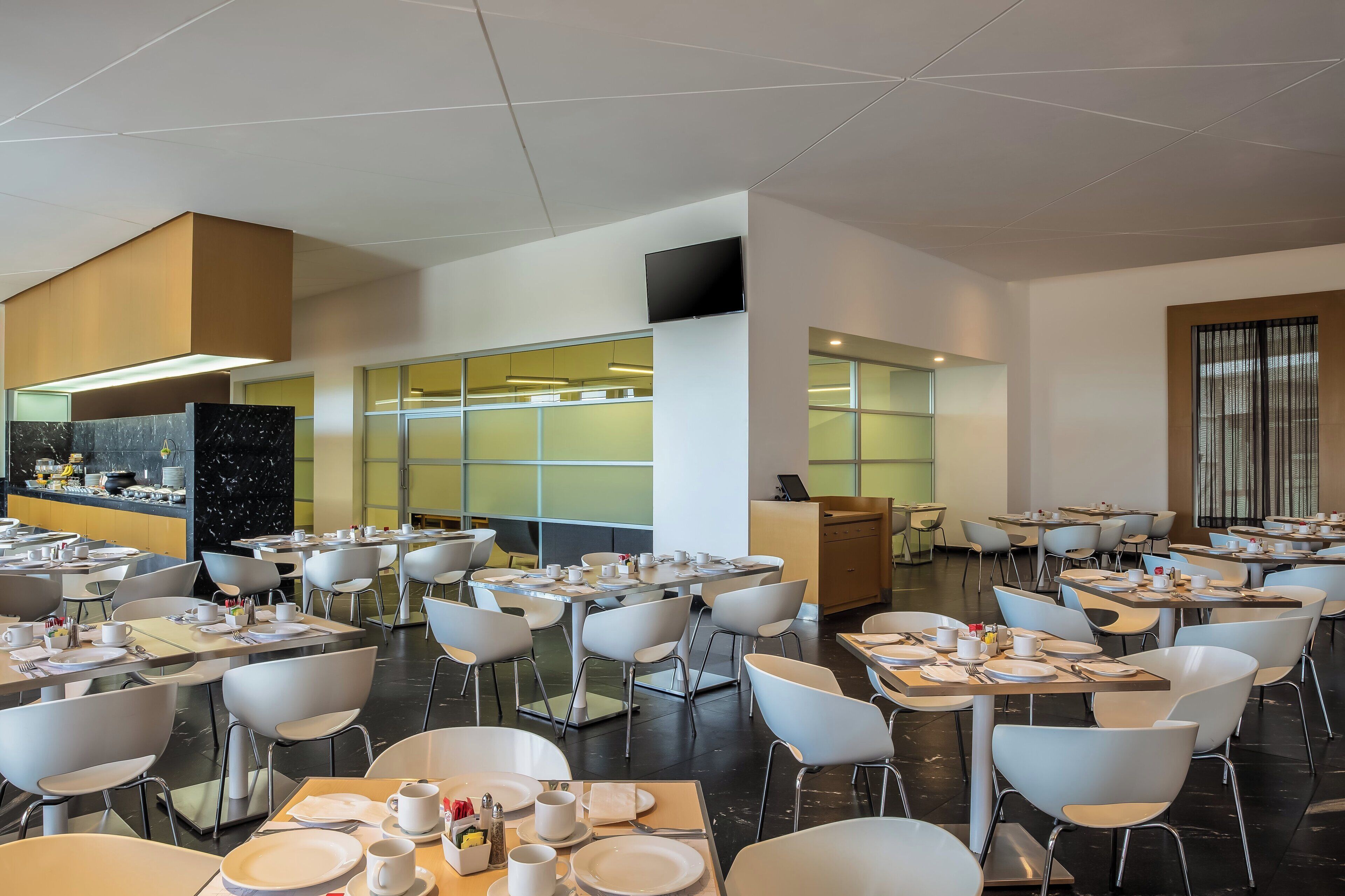 A modern dining area with tables and chairs, a kitchen area, and a large window.