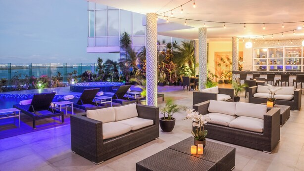 A rooftop bar with outdoor seating, a pool, and a bar area with a view of the city skyline.