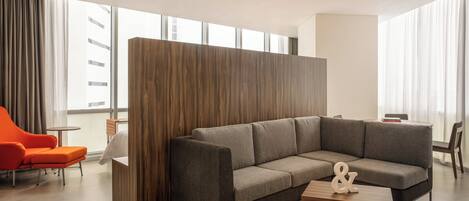 Una sala moderna con un sofá seccional, un panel de madera decorativo, una mesita y vistas luminosas al exterior.