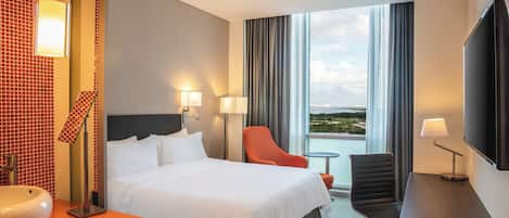 A hotel room with a bed, two chairs, a desk, a TV, and a large window with a view.