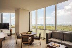 Una habitación de hotel moderna con un ventanal grande, un televisor de pantalla plana, una mesa de comedor redonda y un sofá.