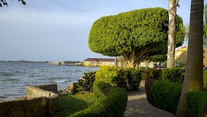 A landscaped pathway beside a body of water, with a well-maintained hedge and a palm tree. - Protea Hotel by Marriott Entebbe (Entebbe)
