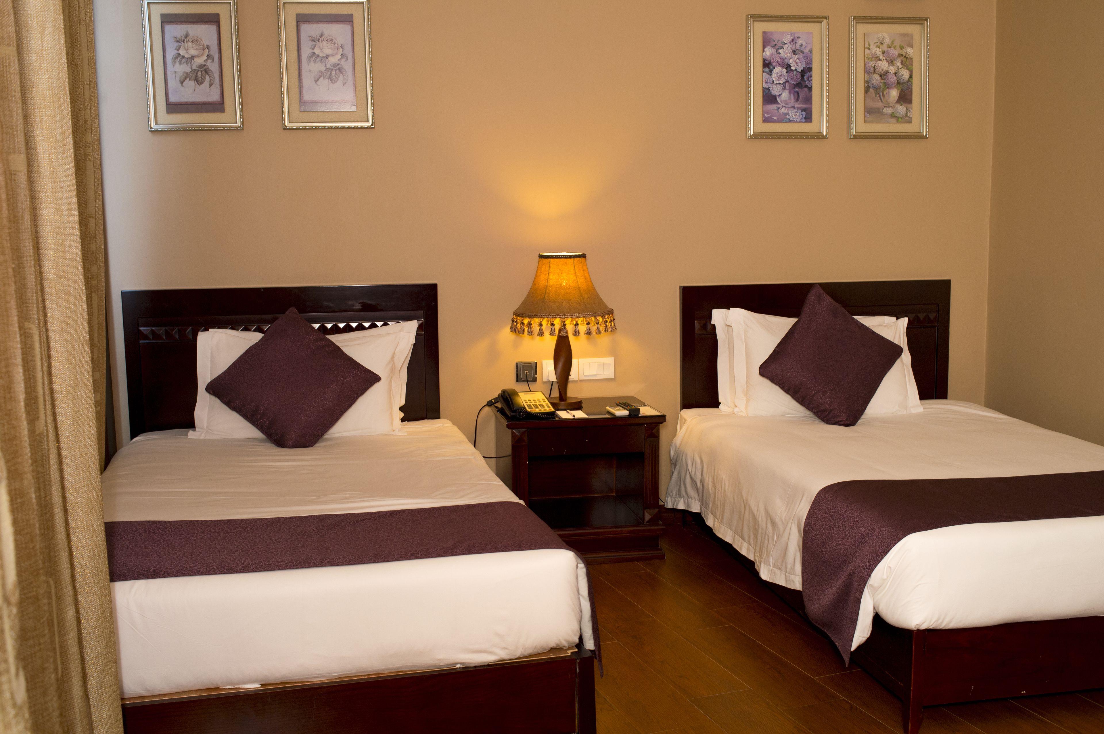 Une chambre d’hôtel avec deux lits, une table de chevet avec une lampe et des œuvres d’art florales encadrées accrochées au mur.
