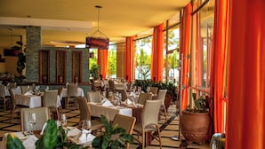 A restaurant with multiple tables and chairs, large windows with curtains, and potted plants. - Protea Hotel by Marriott Entebbe (Entebbe)