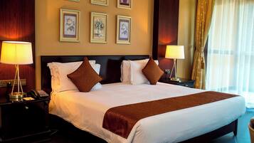 Habitación de hotel con una cama grande, dos mesitas de noche, lámparas, cuadros en la pared y un ventanal con cortinas.