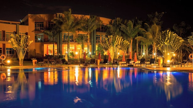 A nighttime view of a hotel pool area with a reflection of the building and palm trees. - Protea Hotel by Marriott Entebbe (Entebbe)