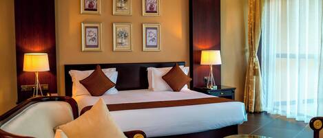 A hotel room with a large bed, two bedside tables, a glass coffee table, and a view of the outdoors.