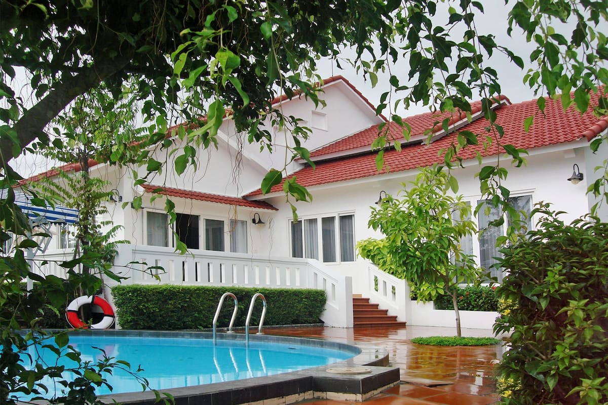 A white building with a red-tiled roof, a swimming pool, and a staircase leading to the entrance.