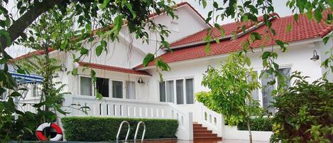 A white building with a red-tiled roof, a swimming pool, and a staircase leading to the entrance.