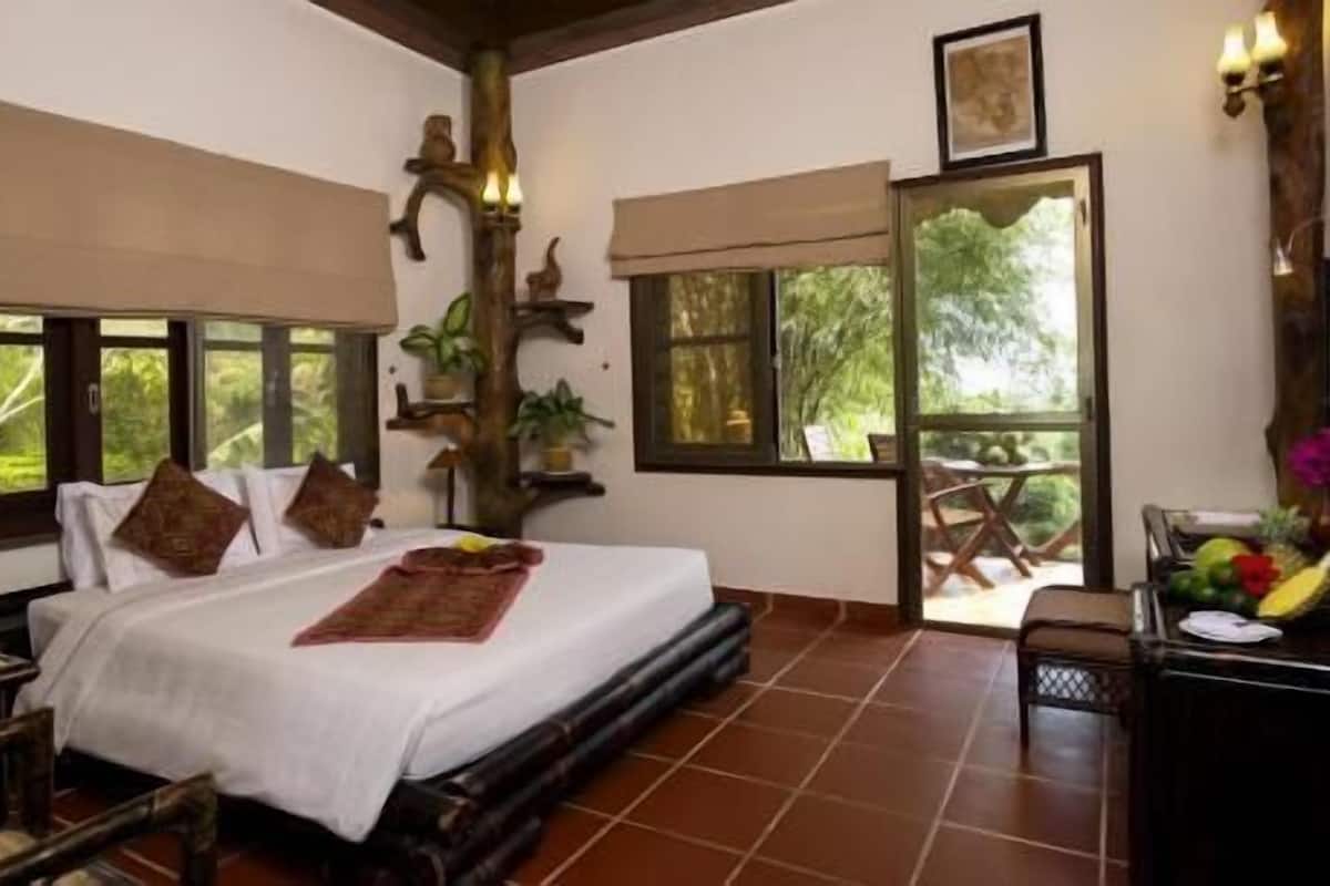 A bedroom with a bed, pillows, a bedside table, a window, and a view of the outdoors.