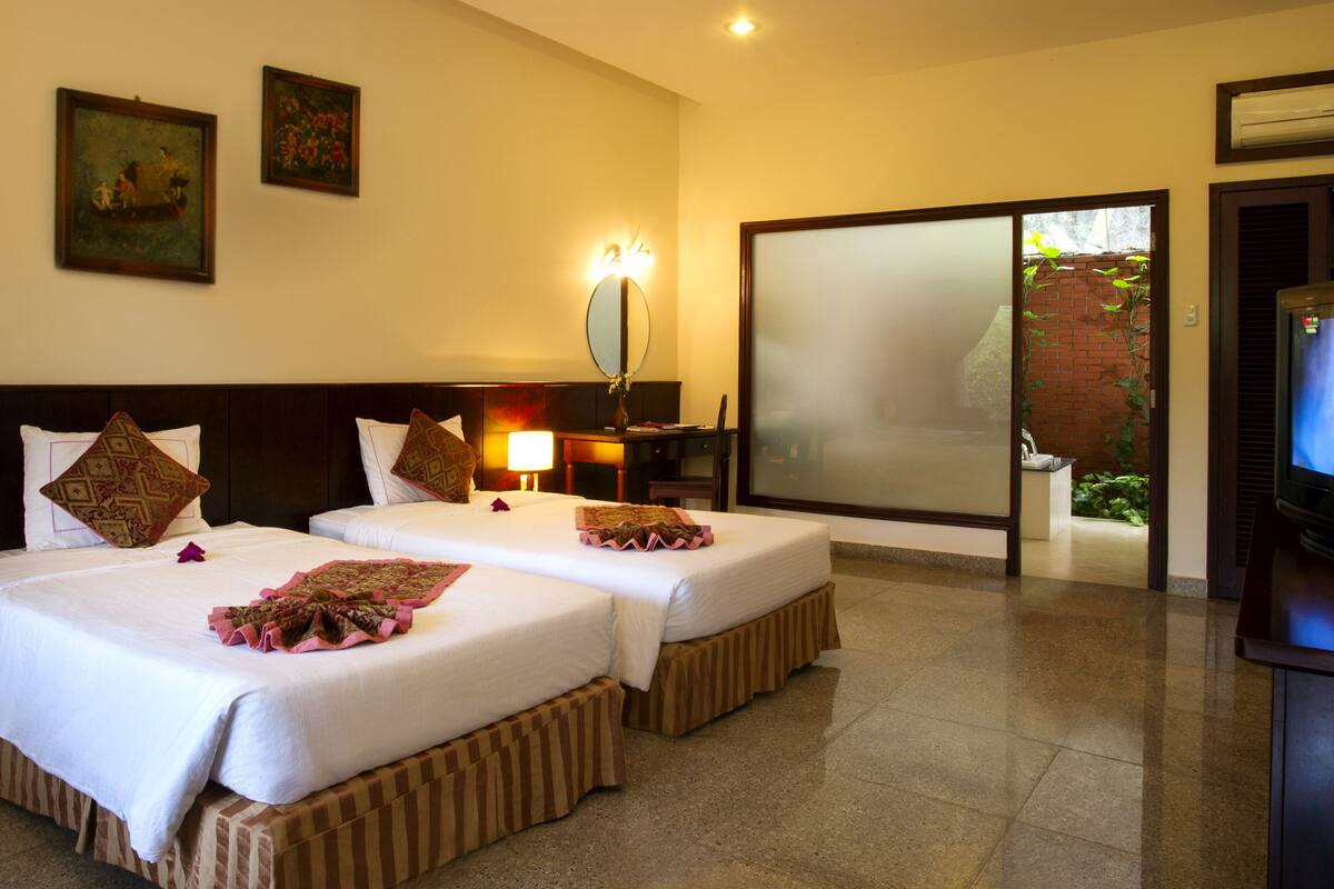 A hotel room with two beds, a TV, a desk with a phone, and a large window.