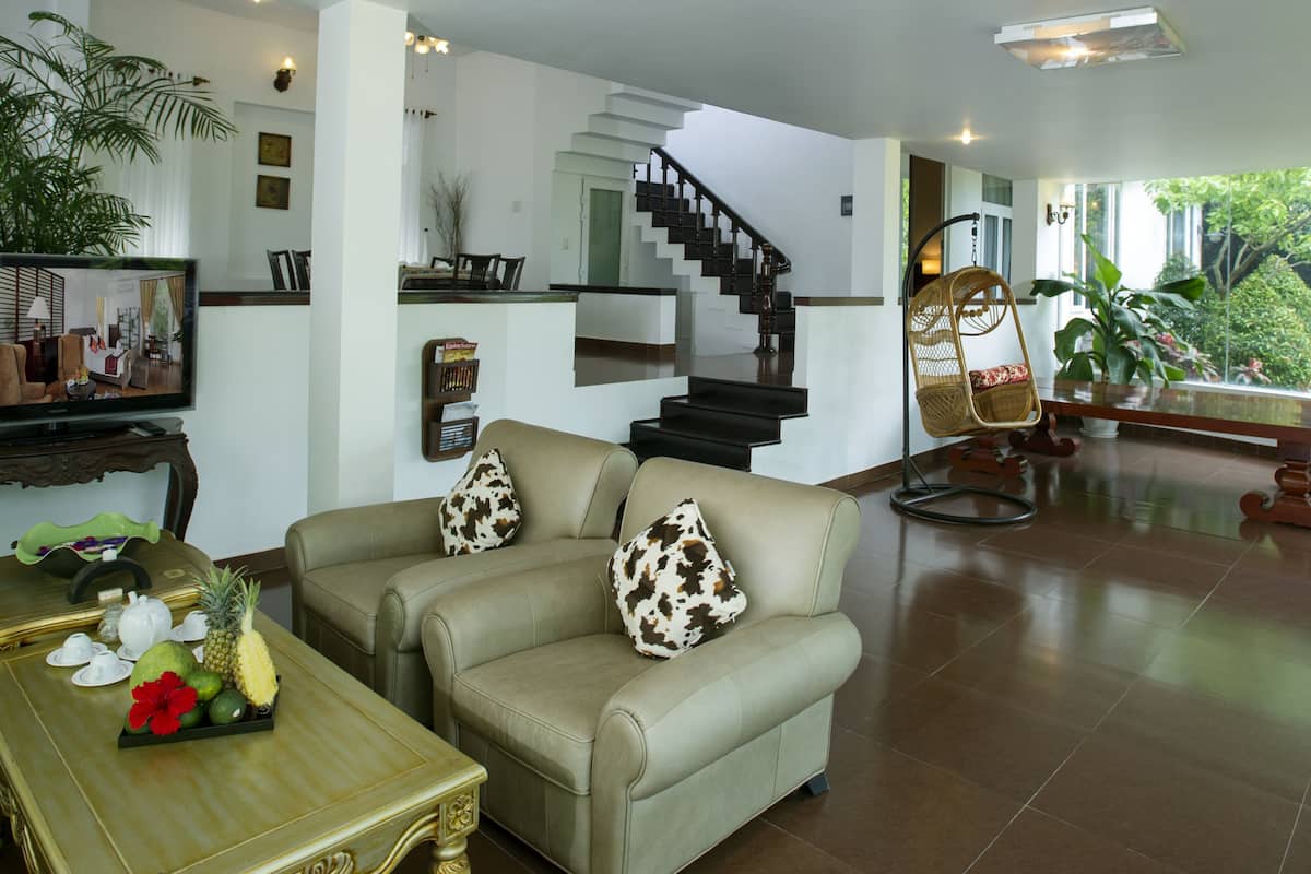 A spacious living area with a sofa, a coffee table with fruit, a wicker chair, and a staircase leading to another level.