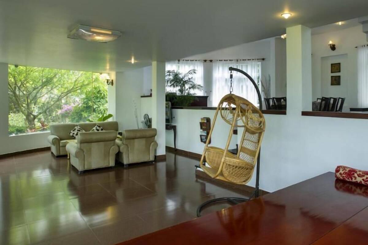A spacious living area with a large window, two sofas, a wicker chair, and a wooden table.