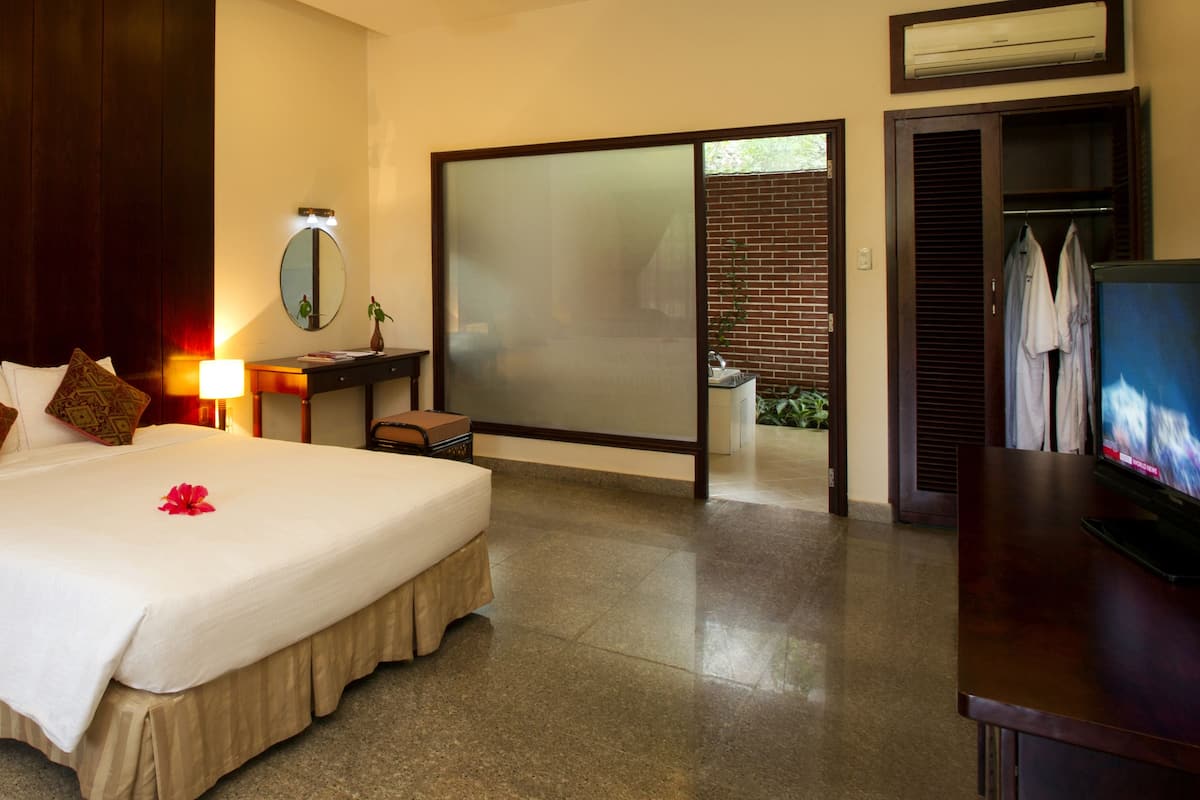 A hotel room with a large bed, bedside lamps, a TV, a mirror, and a sliding door leading to a balcony.
