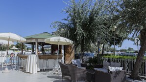 An outdoor patio with wicker furniture, umbrellas, and a bar area. - Hotel Silver (Cesenatico)