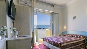 A hotel room with a bed, a desk, a TV, a window with a view of the beach, and a small religious icon on the wall. - Hotel Silver (Cesenatico)