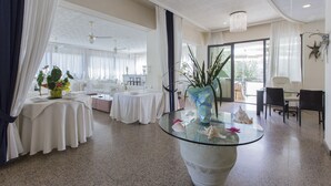 A spacious hotel lobby with a round glass table, white curtains, and a large window offering a view of the outdoors. - Hotel Silver (Cesenatico)