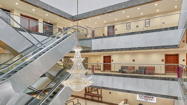 A multi-level hotel lobby with a central atrium, escalators, seating areas, and a reception desk. - Makarem Al Bait Hotel (Makkah)