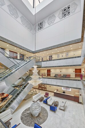 Eine mehrstöckige Hotelhalle mit einem zentralen Atrium, Rolltreppen, Sitzbereichen und einer Rezeption.