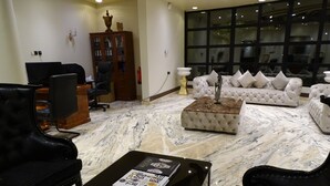 Ein geräumiges Wohnzimmer mit Marmorboden, einer weißen Sofagarnitur, einem schwarzen Ledersessel und einem Couchtisch mit Büchern.