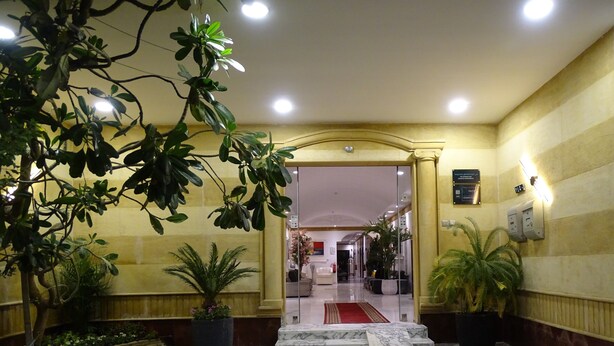Eine Hotellobby mit Marmorboden, Topfpflanzen und einem roten Teppich, der zum Empfangsbereich führt.