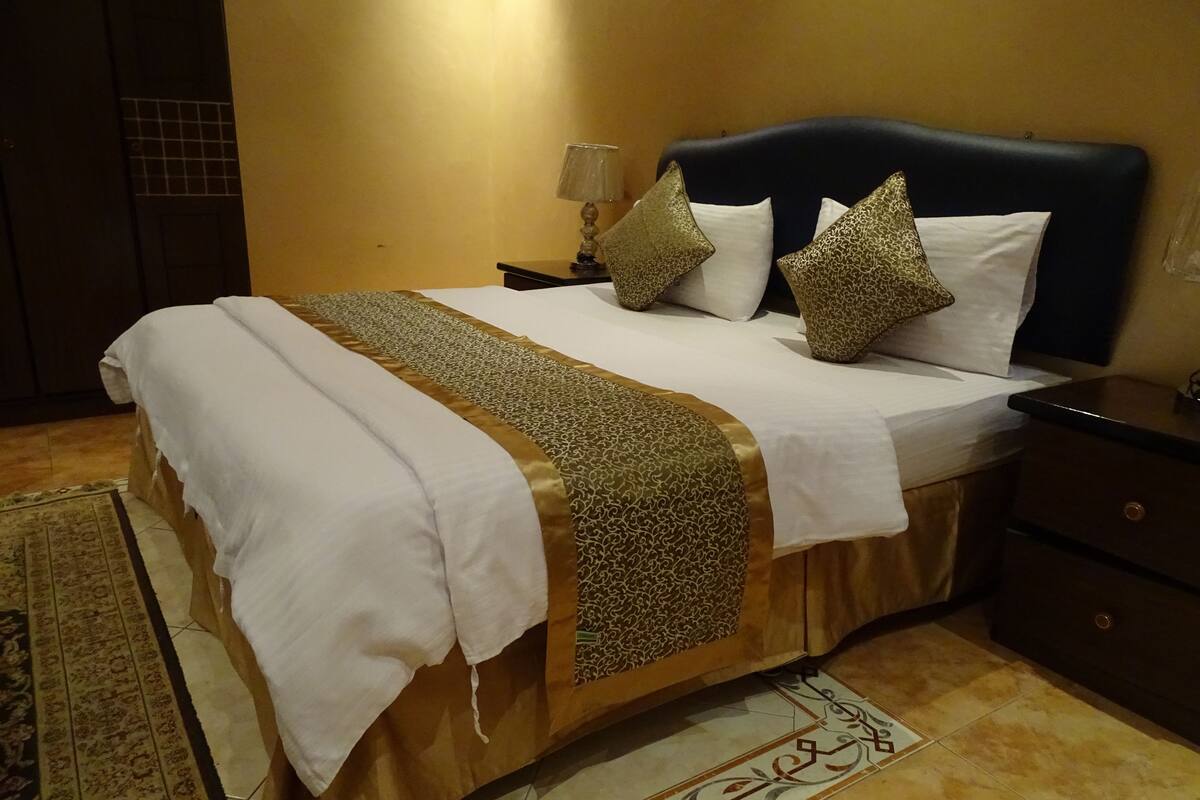 A neatly made bed with a patterned bedspread, a dark headboard, and decorative pillows.