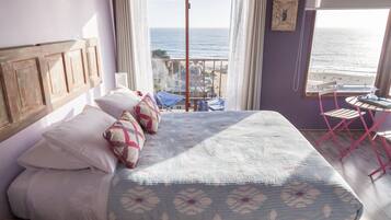 Un dormitorio con cama, almohadas, vista al mar, un balcón y una mesa con sillas.