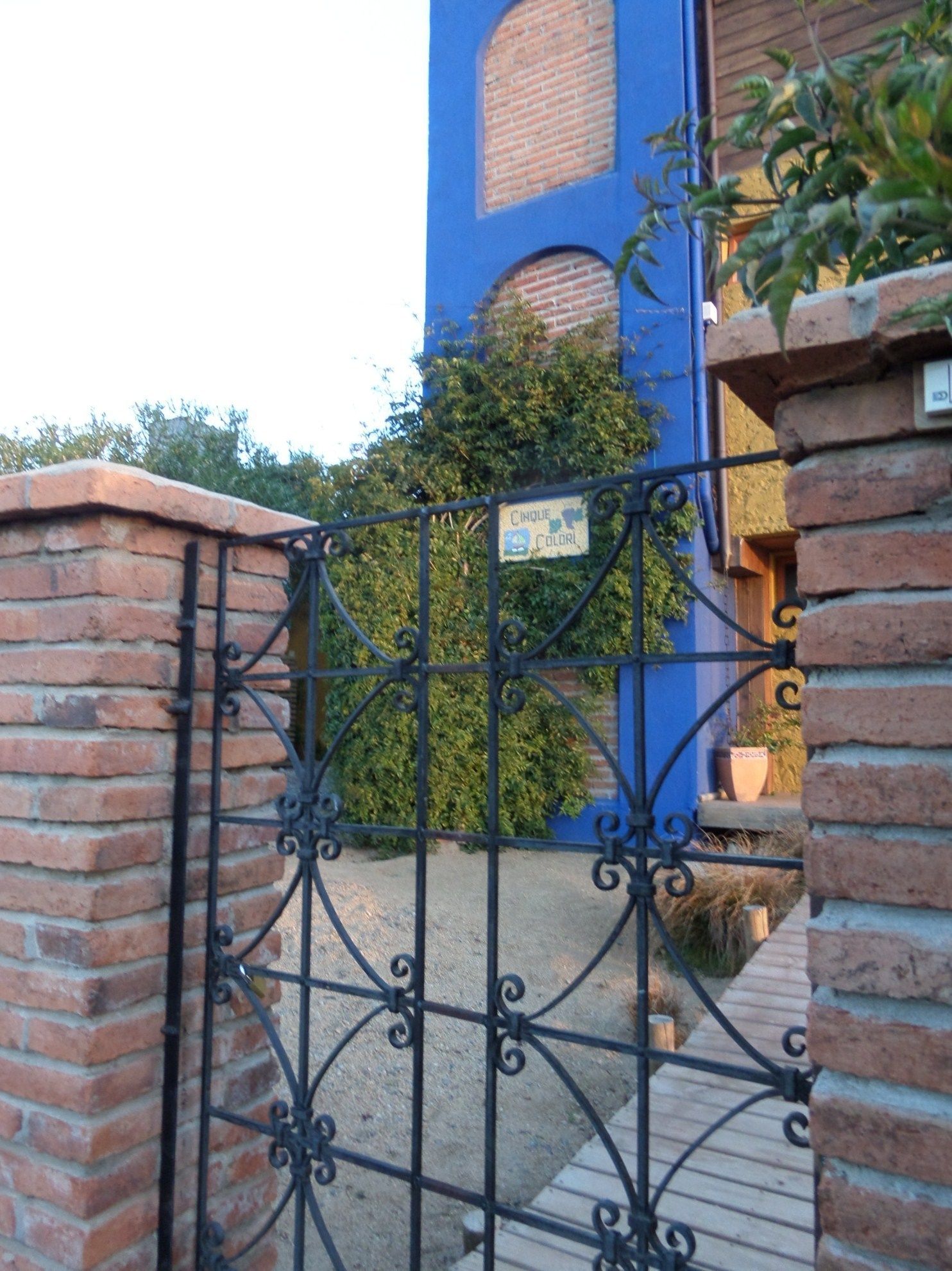 Une porte en métal, sur laquelle on peut lire l’inscription « CINQUE COLORI », se trouve devant un bâtiment bleu aux murs en briques et doté d’une fenêtre.