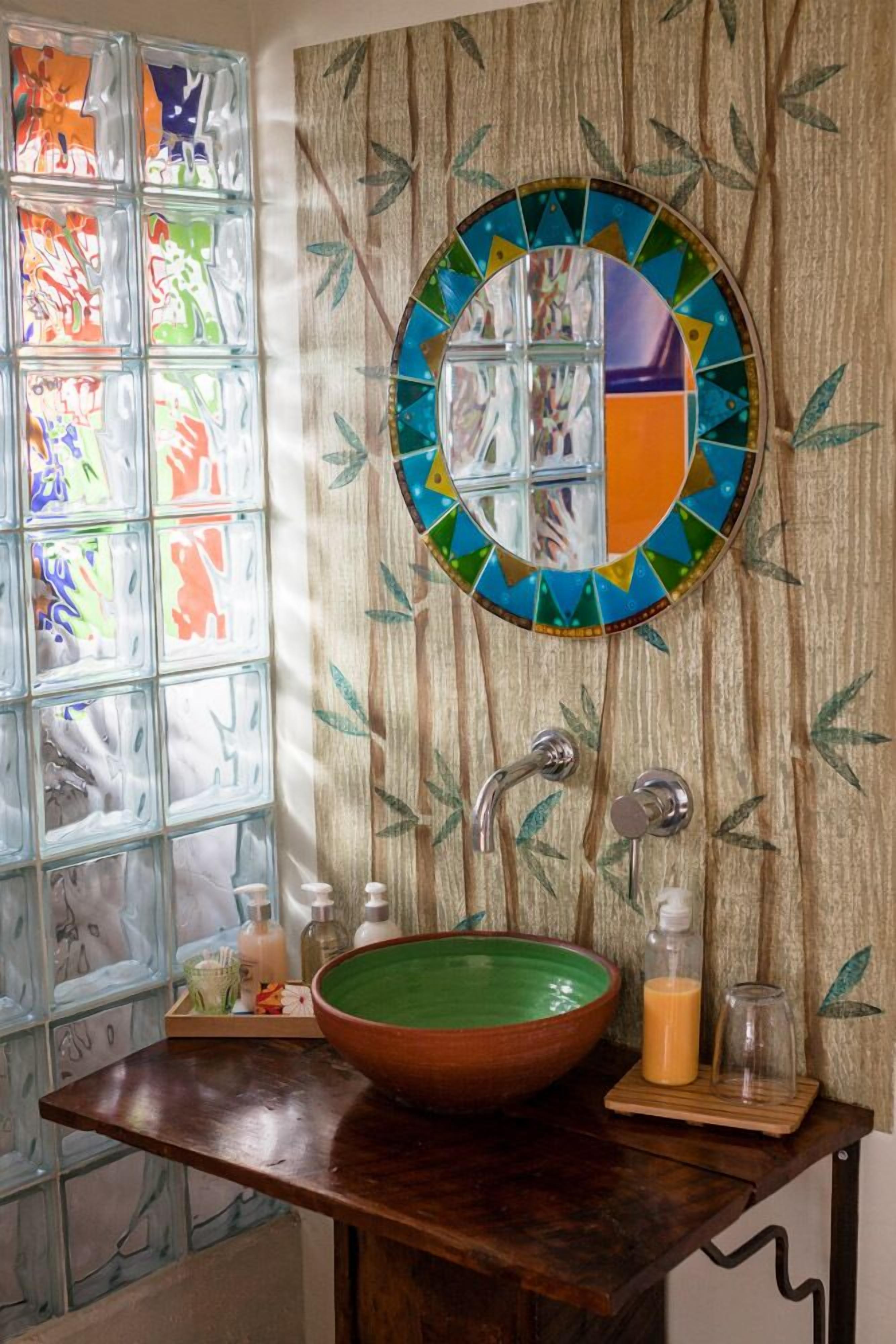A bathroom with a wooden vanity, a green ceramic sink, and a mosaic mirror.