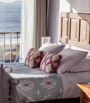Un dormitorio con cama, almohadas, una mesita de noche y vista al mar.