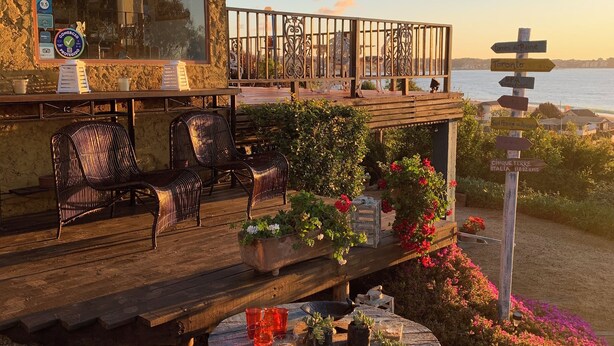 A wooden deck with outdoor seating, a table with drinks, and a signpost with directions. - Cinque Colori (Algarrobo)