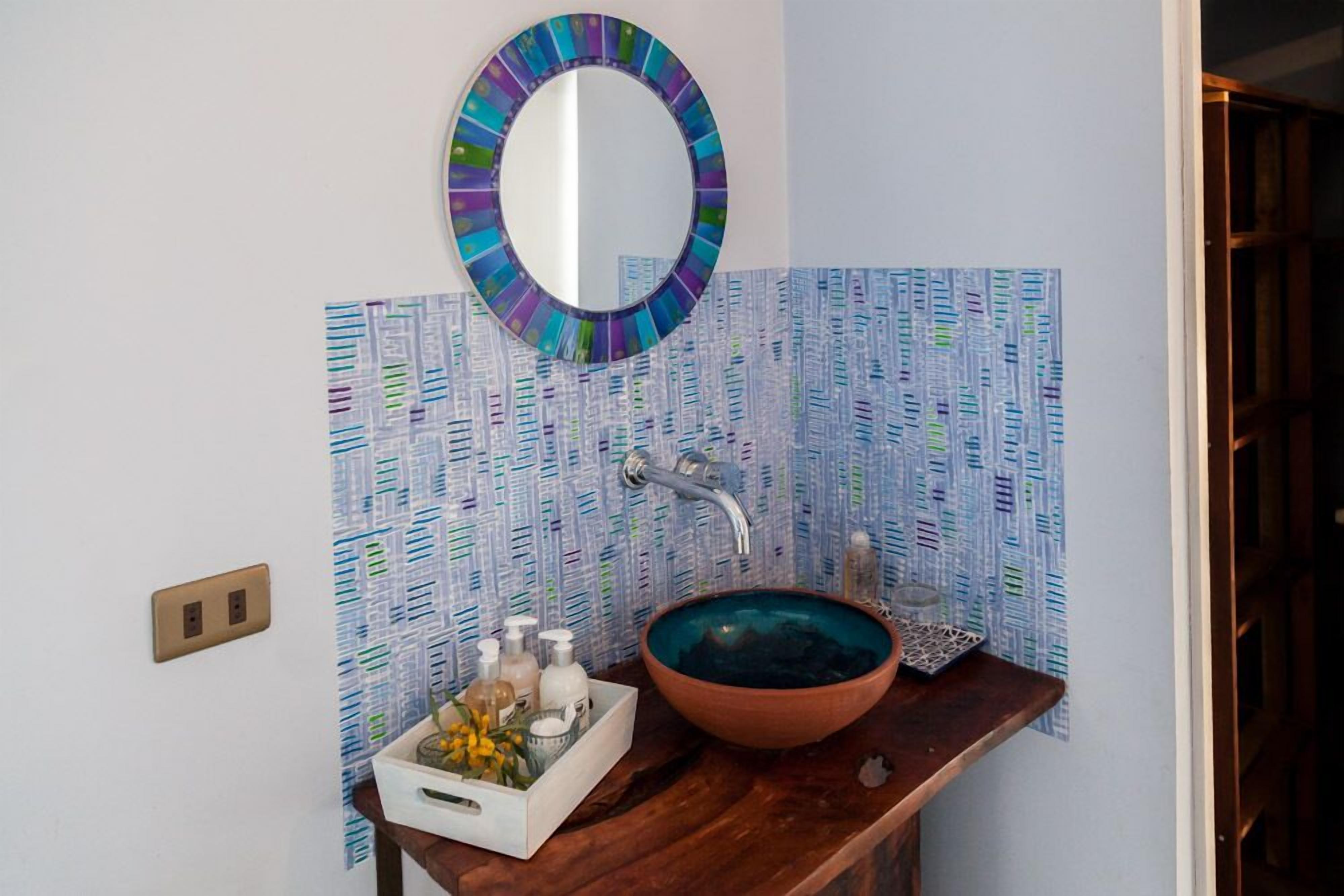 A bathroom with a round mirror, a wooden vanity, a glass bowl sink, and a patterned wall.